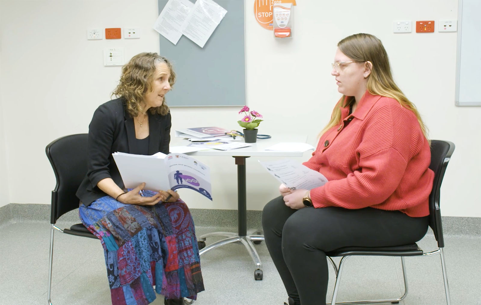 Two women sit in an office looking at a page on a folder