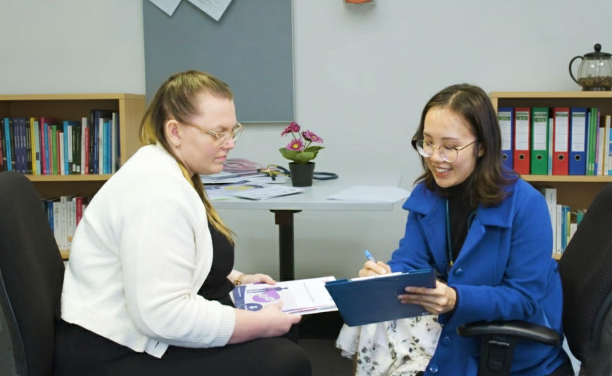 Two women sit in an office looking at a page on a folder
