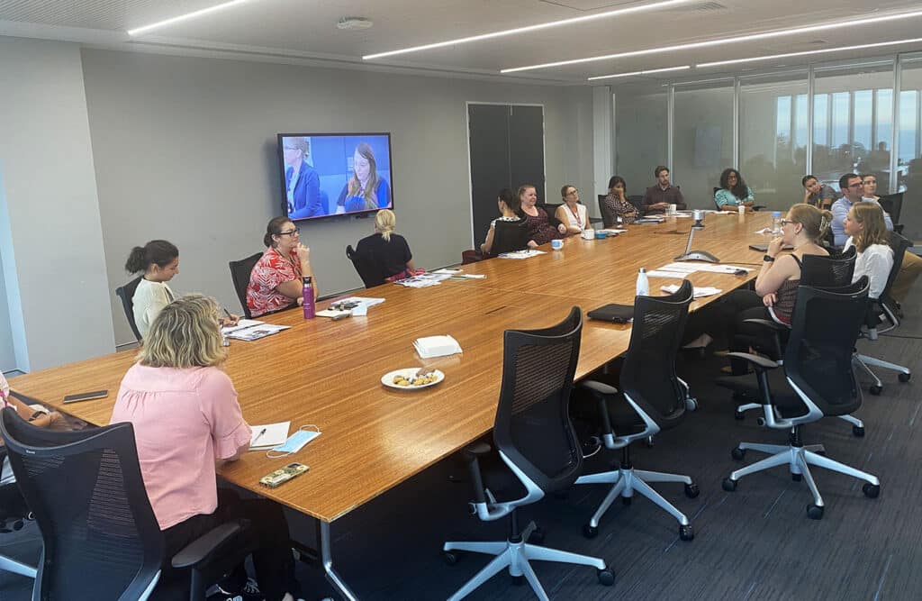 A group of people around a conference table look at a video screen of remote participants