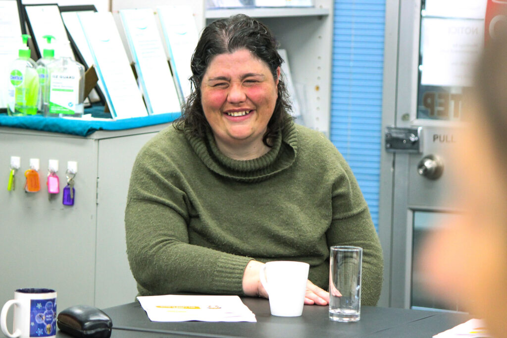 A woman seated at a desk looks at the camera and smiles