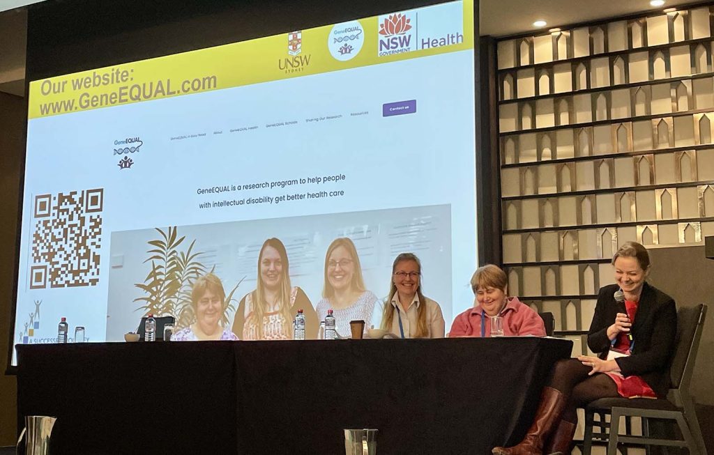 Three women from gene equal present at a table in front of a screen