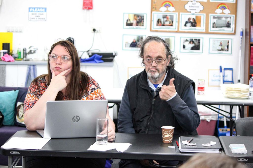 A man and a woman at a conference table. The man gives a thumbs-up signal.