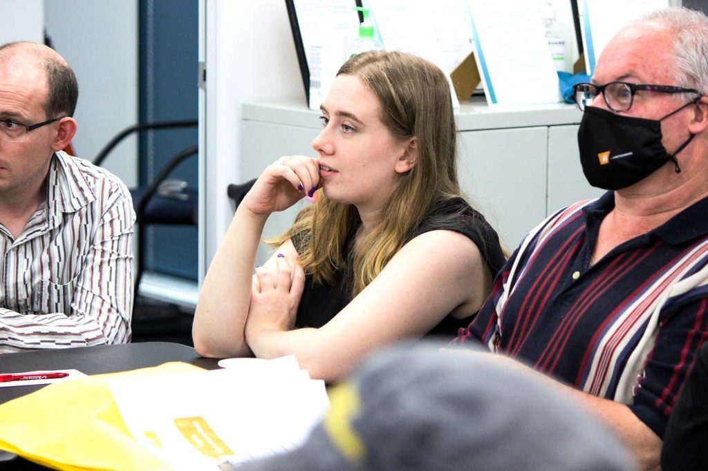 Three people listening to a speaker at a conference table