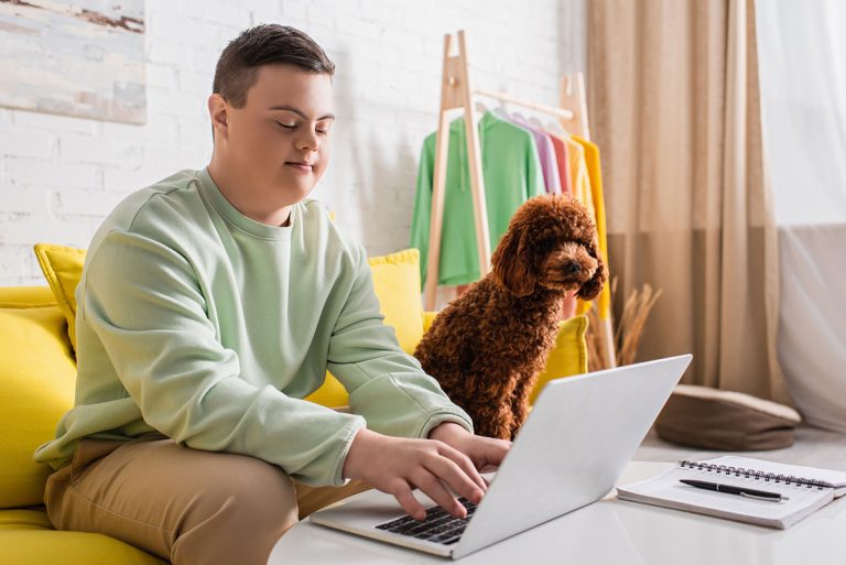 Teenager sitting on couch with poodle and using a laptop